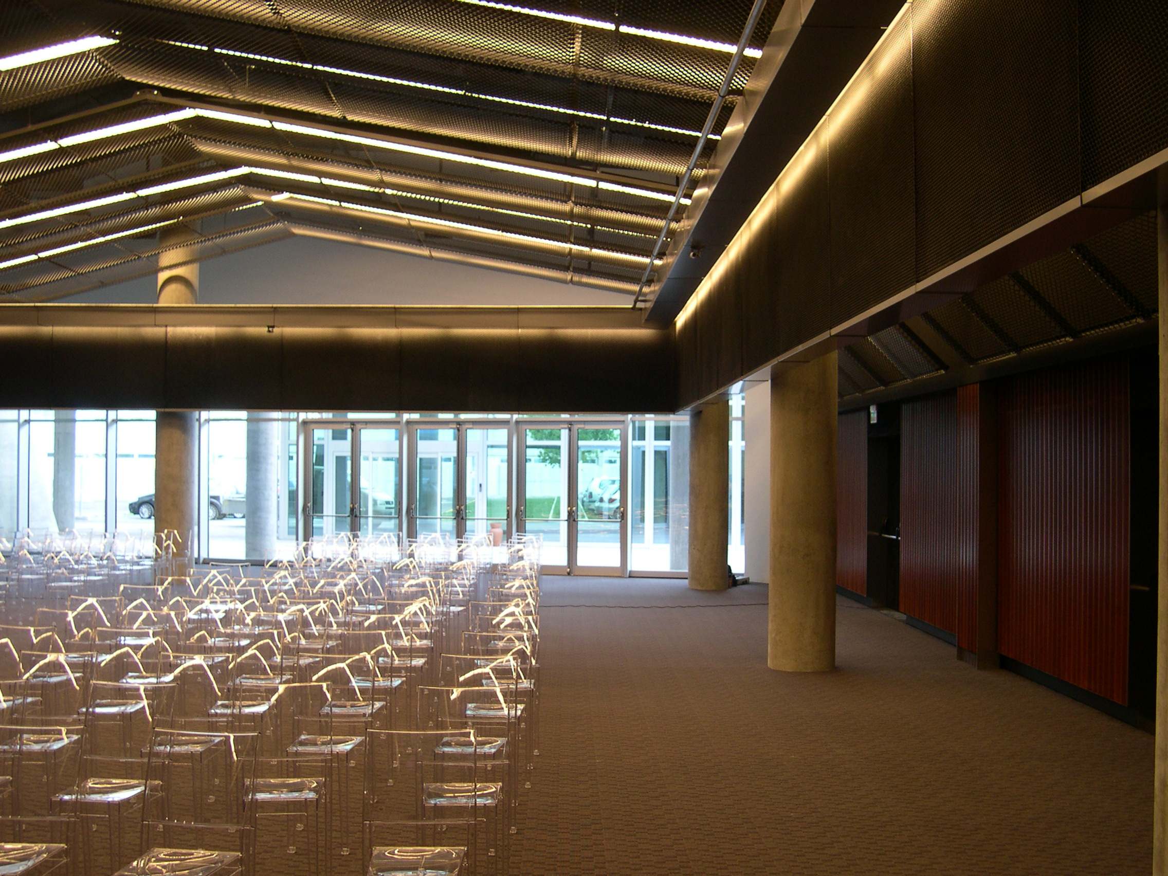 Sala auditorium Hypo Bank Udine con sedie trasparenti, soffitto con travi luminose e vetrate