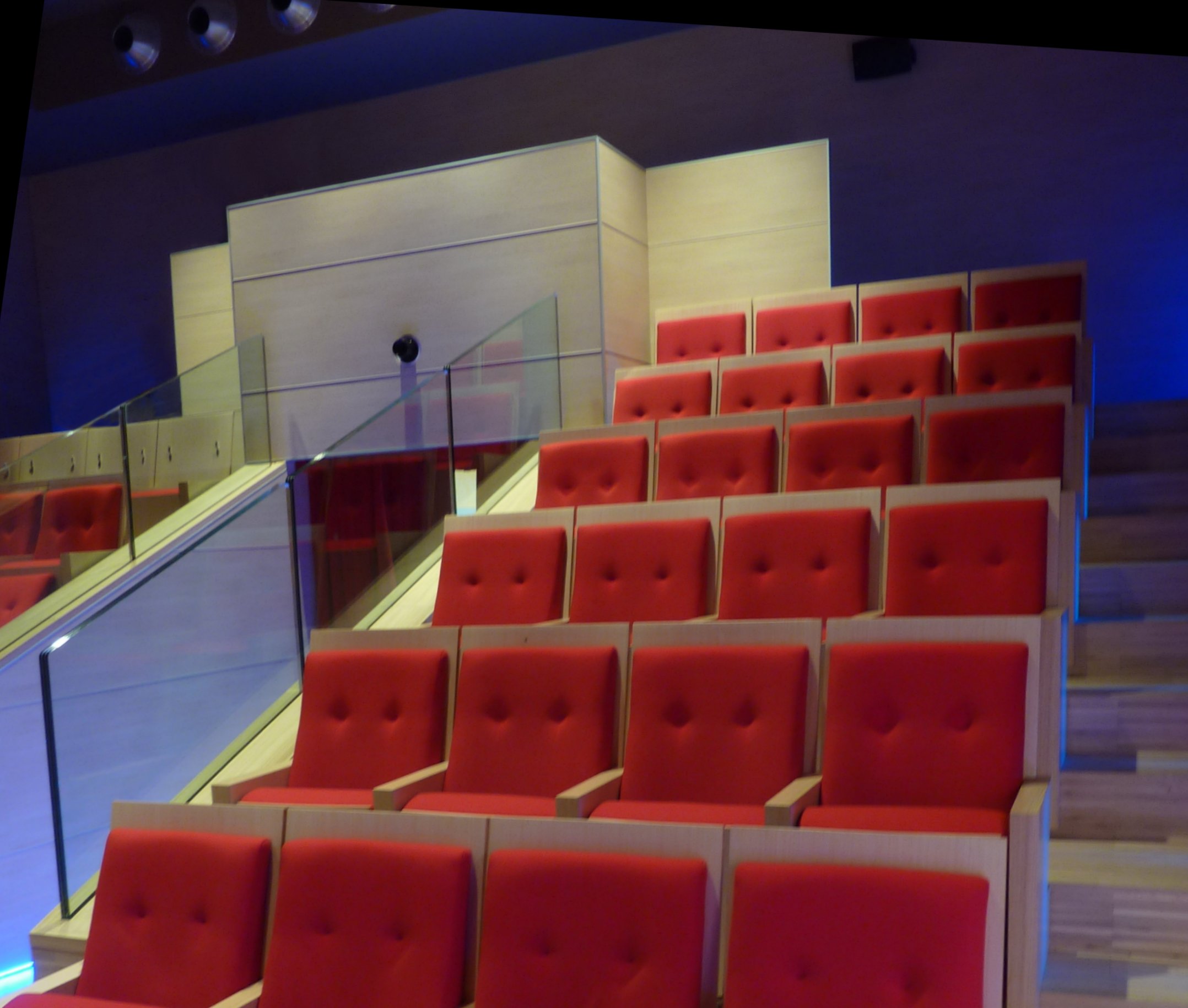 Poltrone rosse imbottite con schienale in legno e ringhiera in vetro nell auditorium di Larido Bleggio