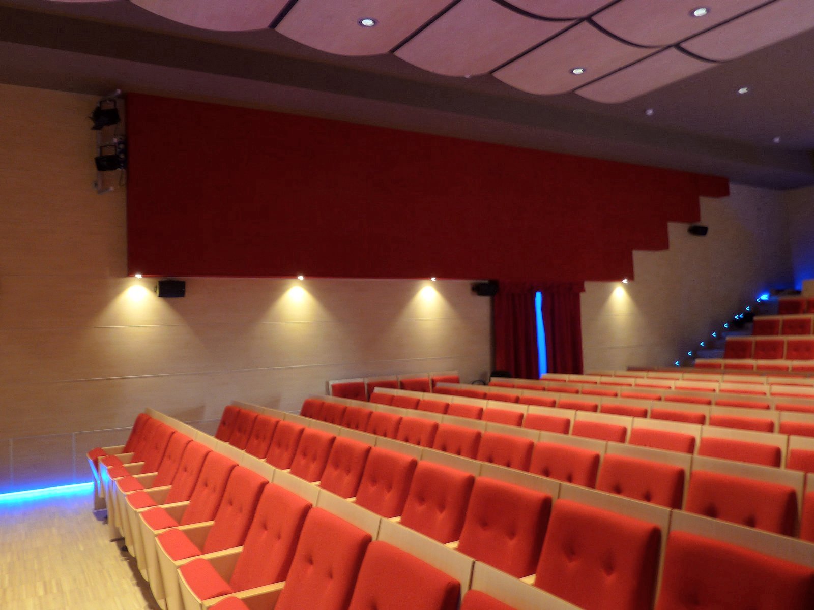 Platea con poltrone rosse, diffusori acustici a parete e illuminazione LED blu nell auditorium di Larido Bleggio