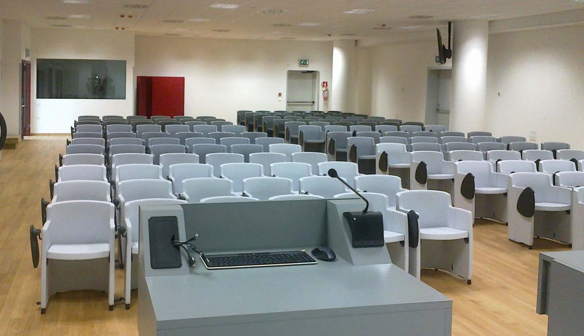 Sala conferenze USSL Feltre vista dal podio con poltrone grigie, postazione relatore con PC e microfono
