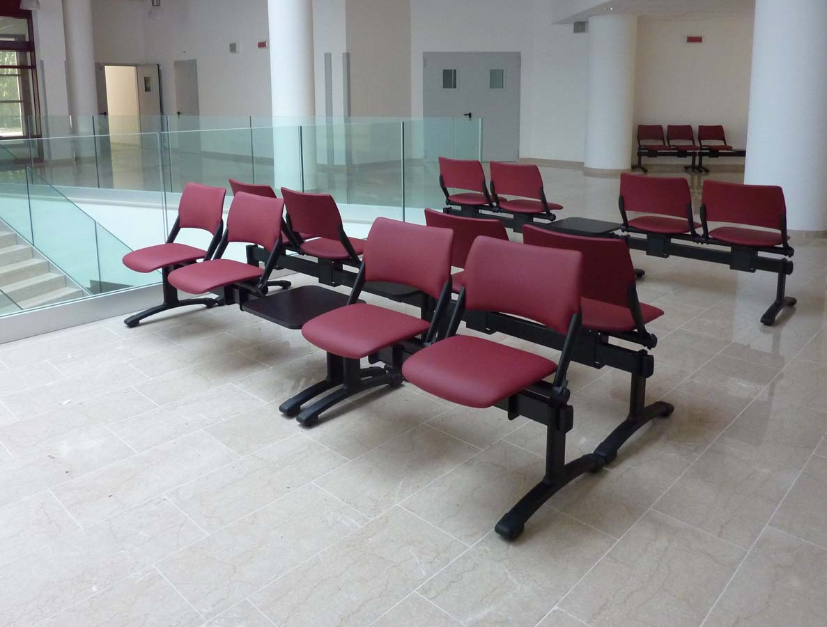 Sedute rosse su trave in area di attesa con ringhiera in vetro presso USSL Feltre
