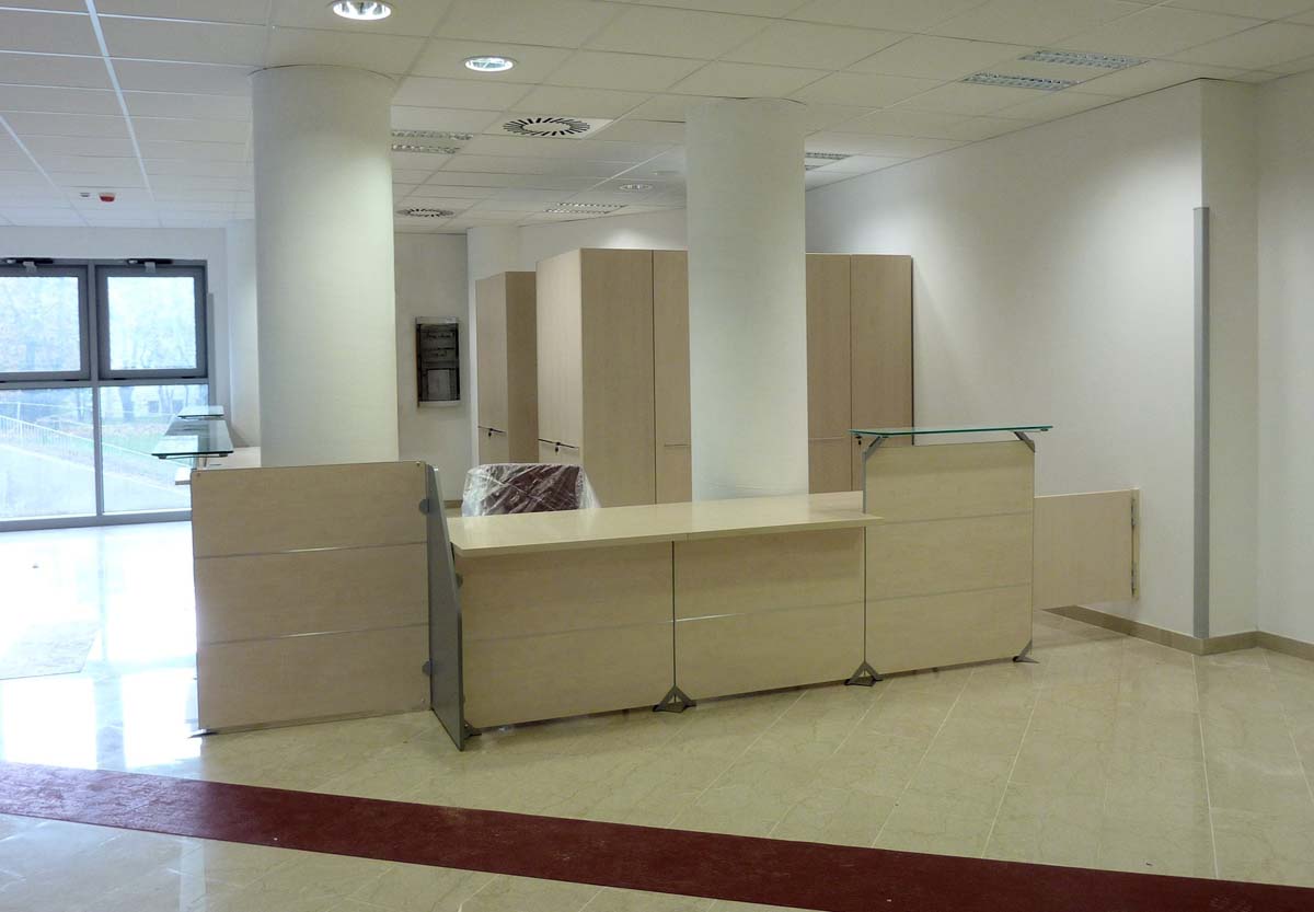 Bancone reception in legno chiaro con armadi e piano in vetro nell area accoglienza USSL Feltre