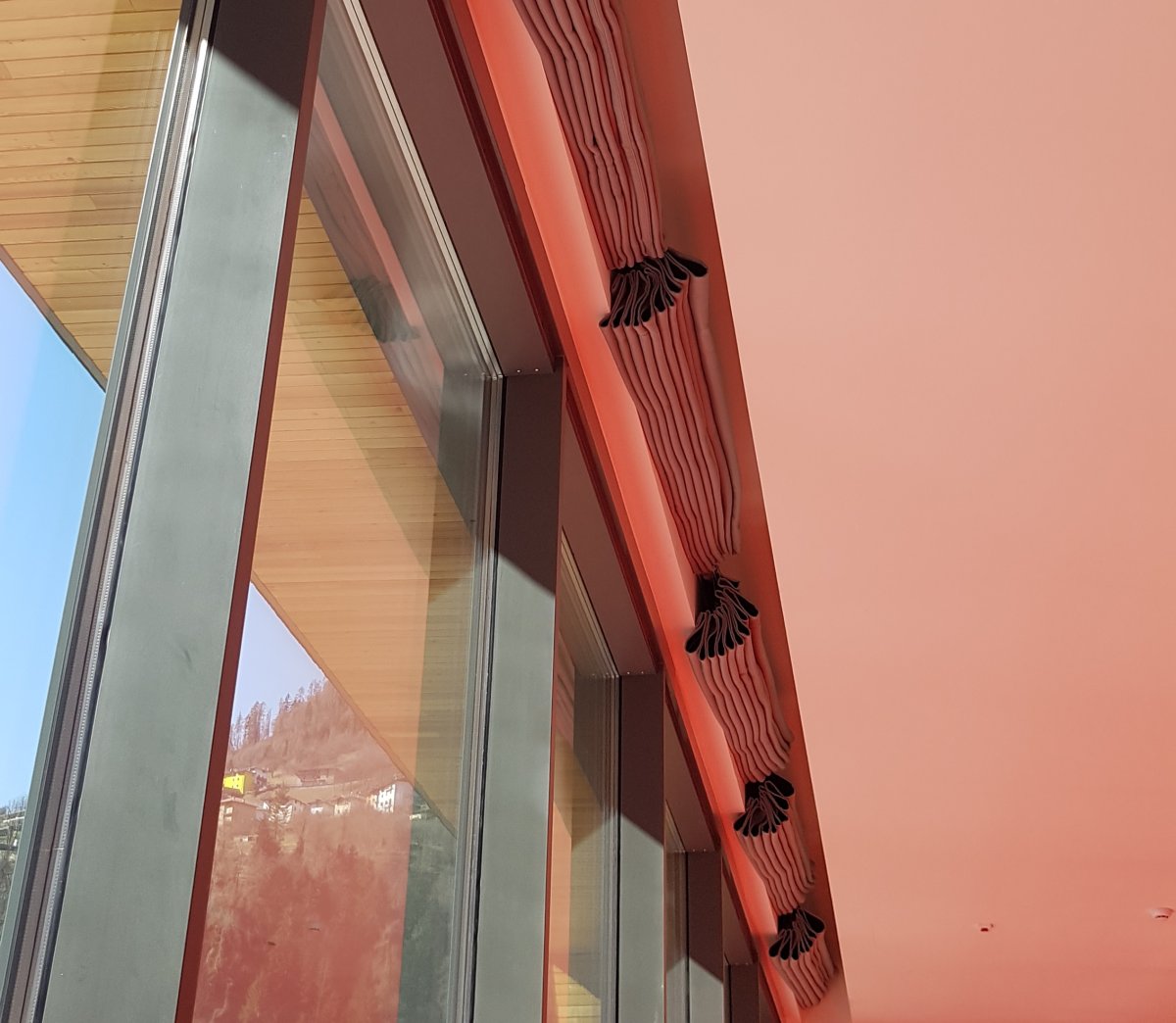 Dettaglio parete rosa con diffusori audio e vetrata al Centro Giovani di Pieve di Bono