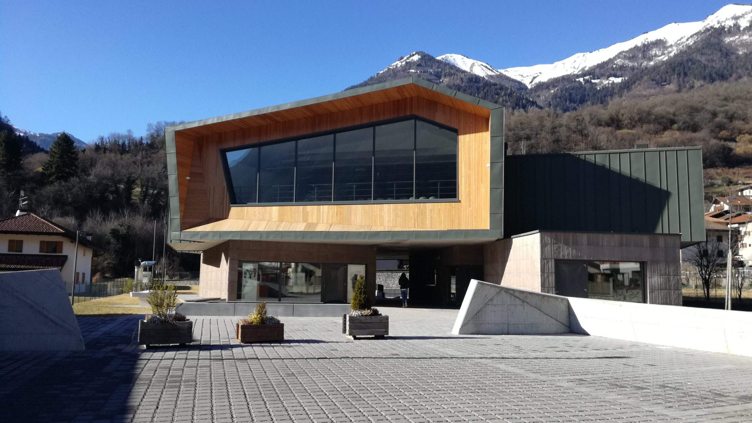 Facciata esterna del Centro Giovani di Pieve di Bono con rivestimento in legno e montagne sullo sfondo