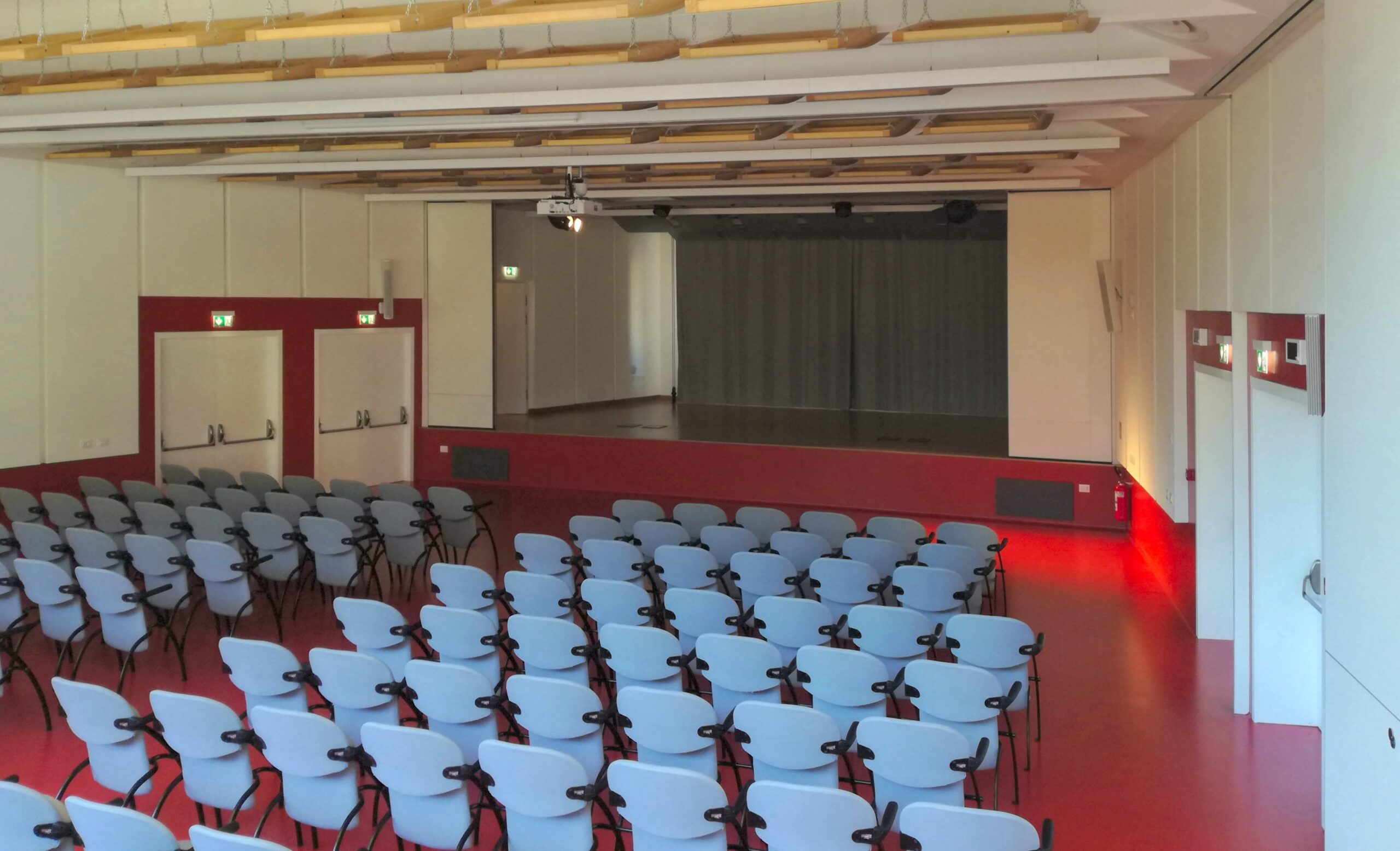 Sala polivalente con sedie grigie, palco e proiettore a soffitto al Centro Giovani di Pieve di Bono