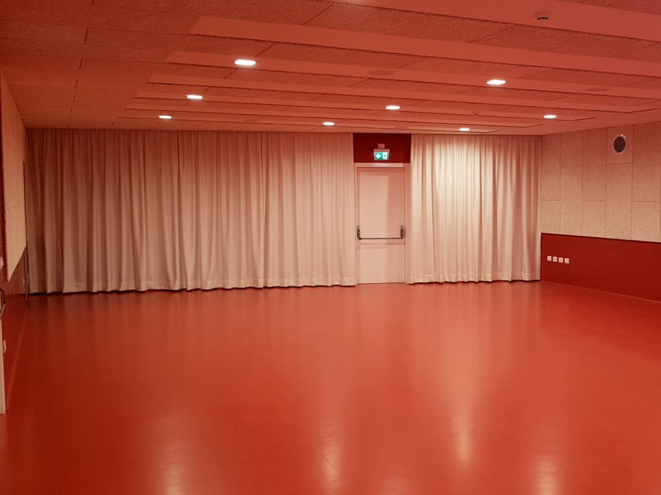 Sala con pavimento rosso e tende oscuranti con pannelli fonoassorbenti al Centro Giovani di Pieve di Bono