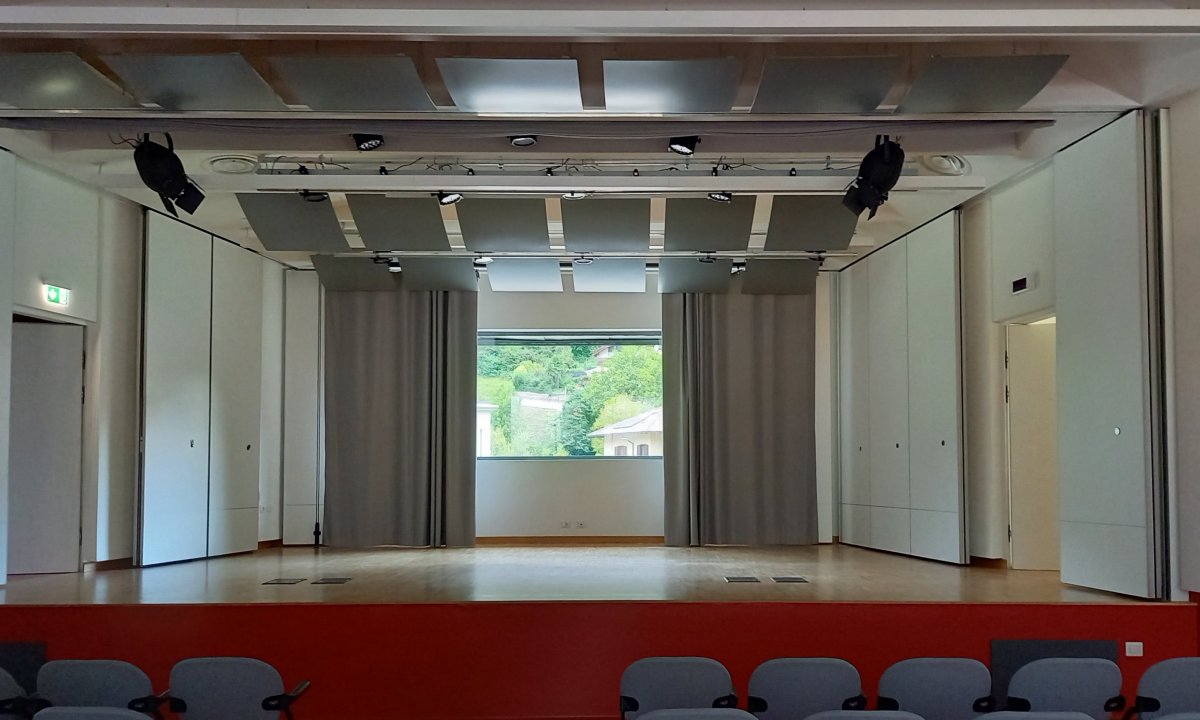 Palco con luci sceniche e tende grigie nella sala del Centro Giovani di Pieve di Bono