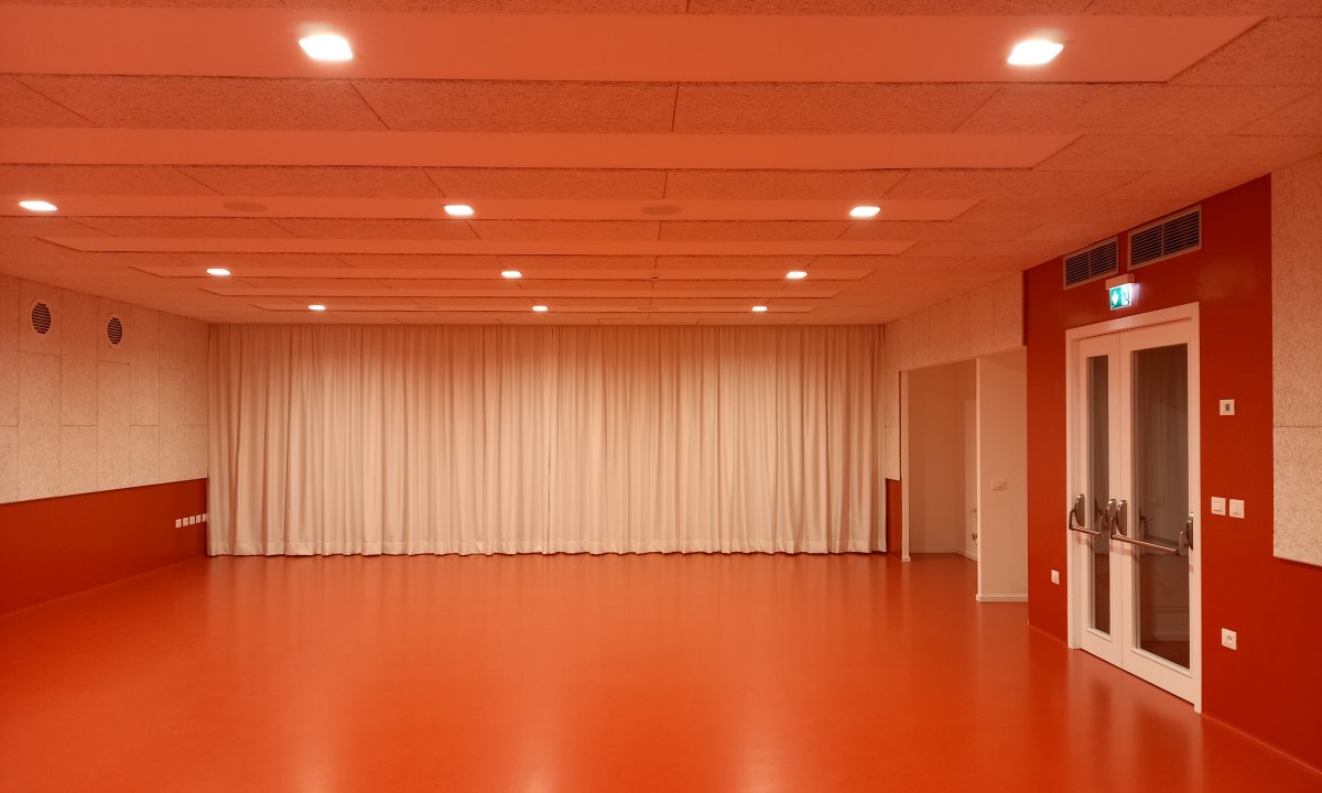 Sala polivalente con pavimento rosso, tende e pannelli fonoassorbenti al Centro Giovani di Pieve di Bono