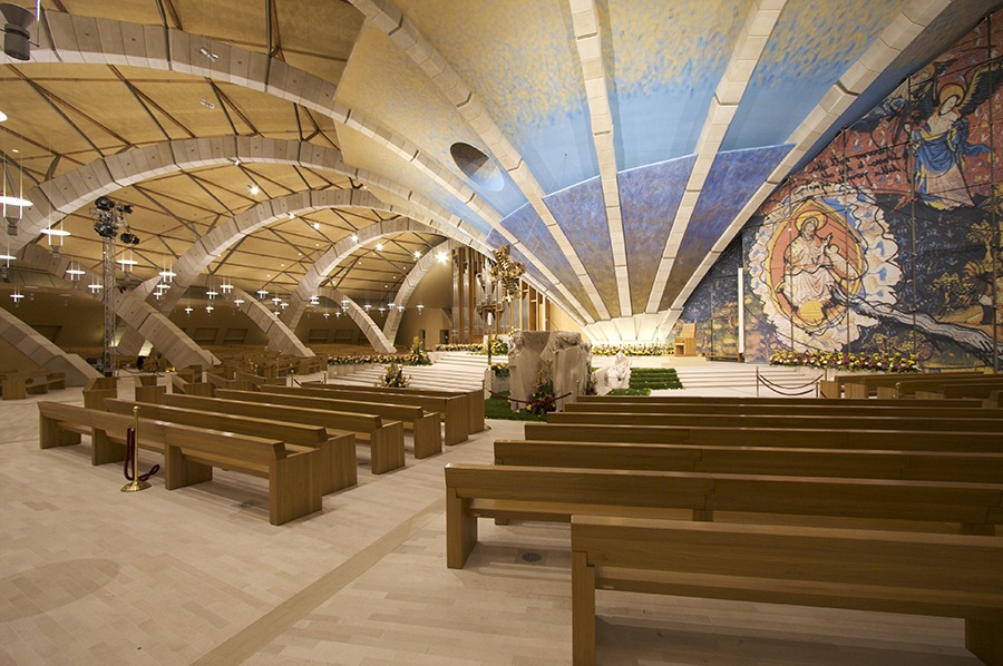 Navata della Chiesa di Padre Pio con panche, archi in cemento, soffitto affrescato e mosaico absidale