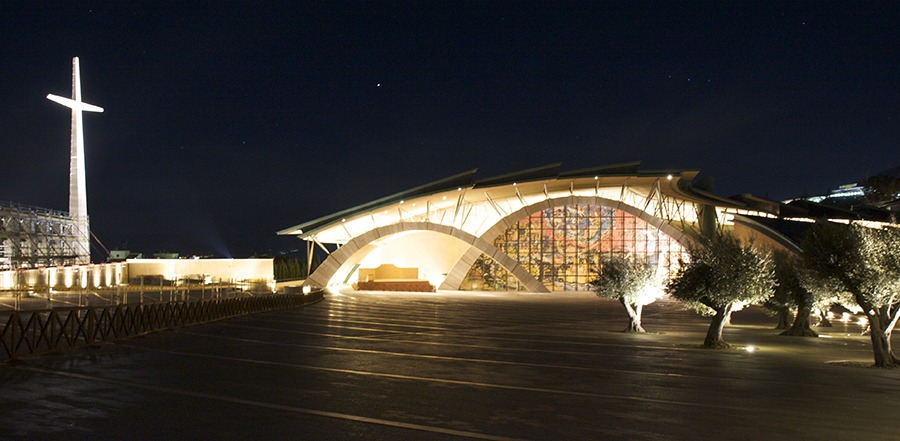 Vista notturna esterna della Chiesa di Padre Pio a San Giovanni Rotondo con croce illuminata e archi