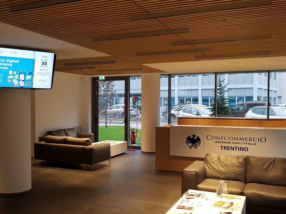 Ingresso della sede Confcommercio Trentino con reception, monitor informativo e divani