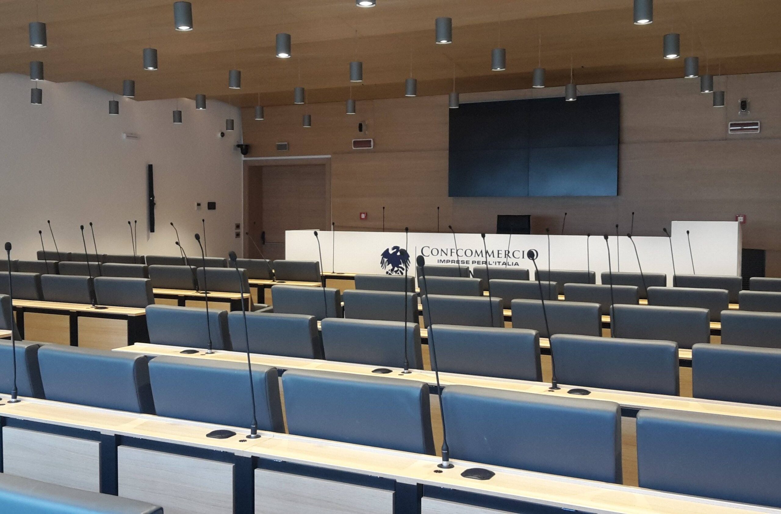 Auditorium Confcommercio Trento con postazioni microfono, schermo e logo sul palco relatori