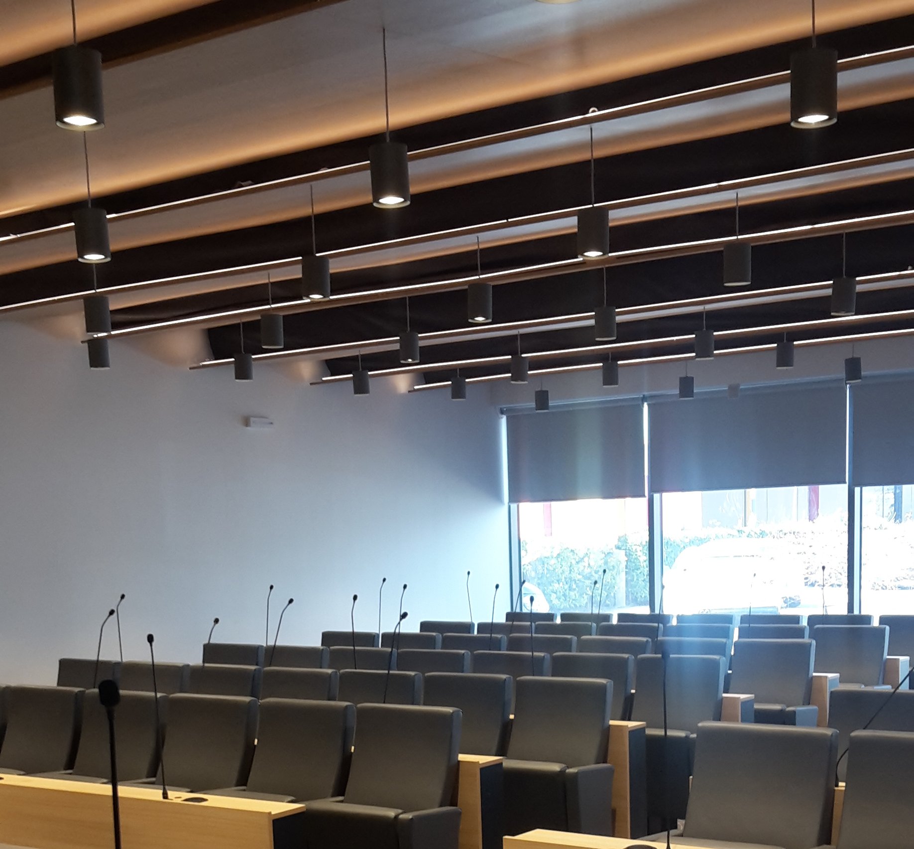 Dettaglio soffitto in legno con faretti cilindrici e postazioni con microfoni nella sala Confcommercio Trento