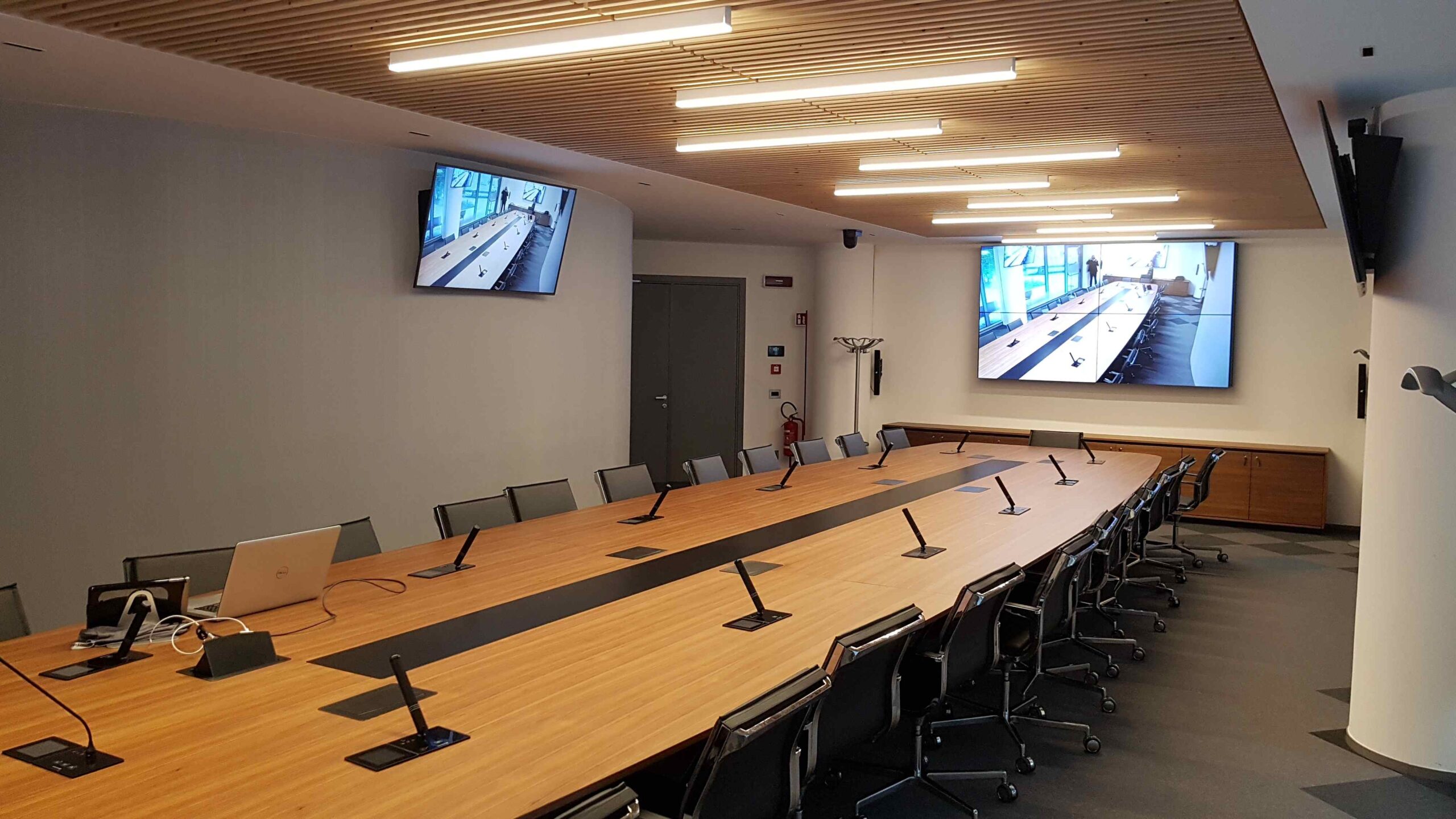 Sala riunioni Confcommercio Trento con tavolo ovale, microfoni e doppio monitor a parete