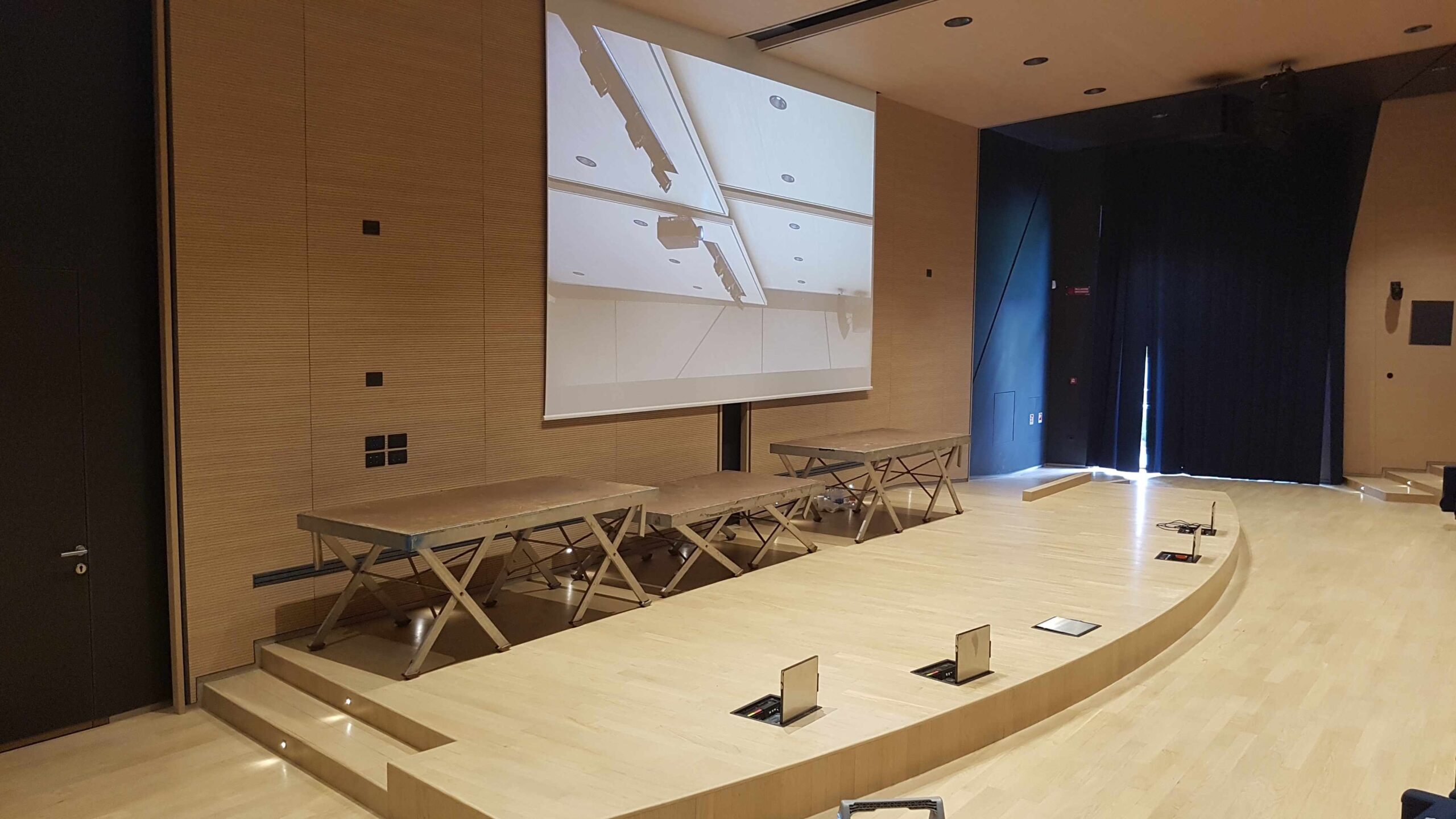 Palco dell auditorium Cooperativa Sant Orsola con schermo proiezione, tavoli relatori e impianto audio