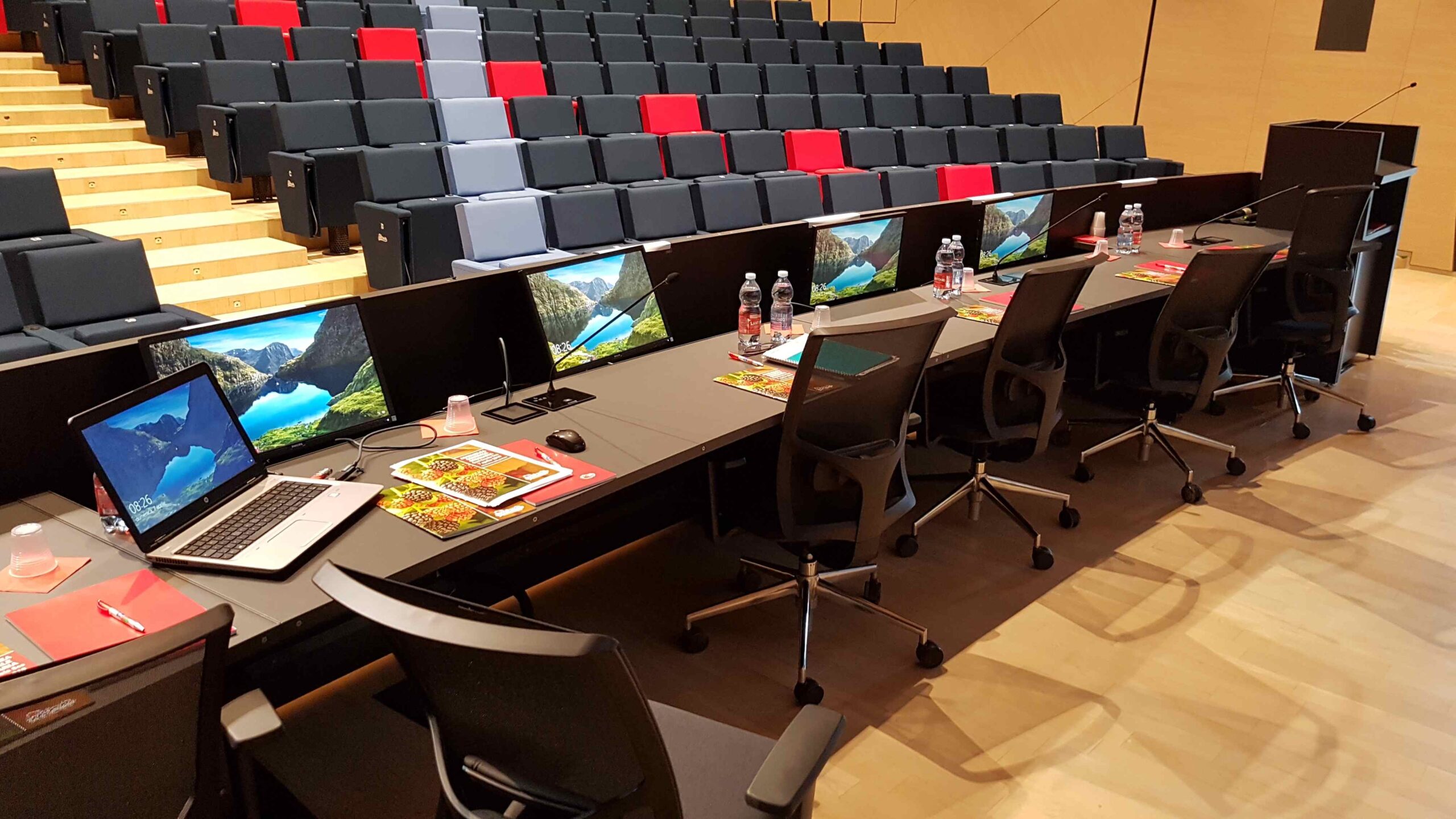 Postazione relatori con monitor, laptop e platea con poltrone nell auditorium Cooperativa Sant Orsola