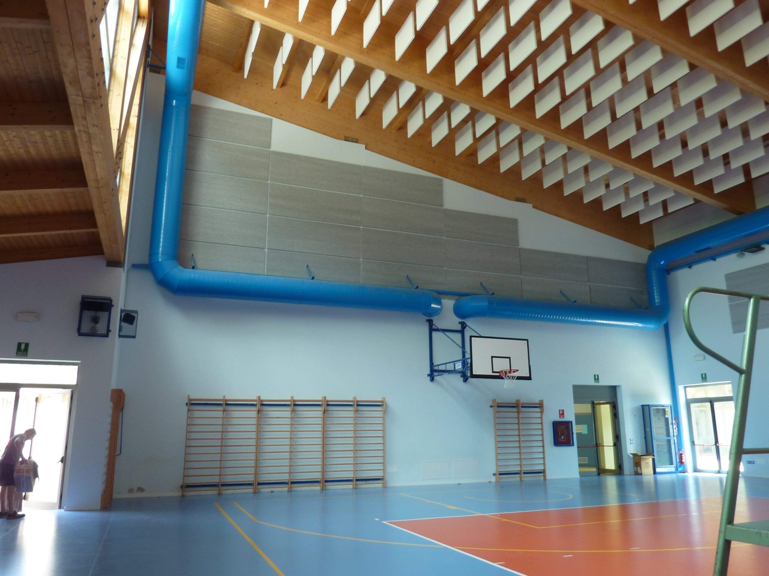 Palestra con pannelli acustici a parete e a soffitto, campo da basket e canestro visibili