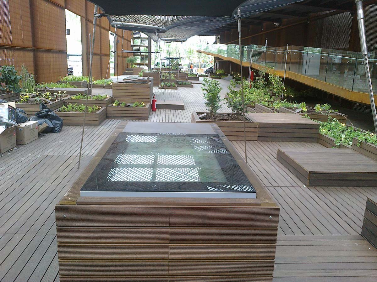 Area esterna del padiglione Expo Milano 2015 con pedane in legno e vasche per piante