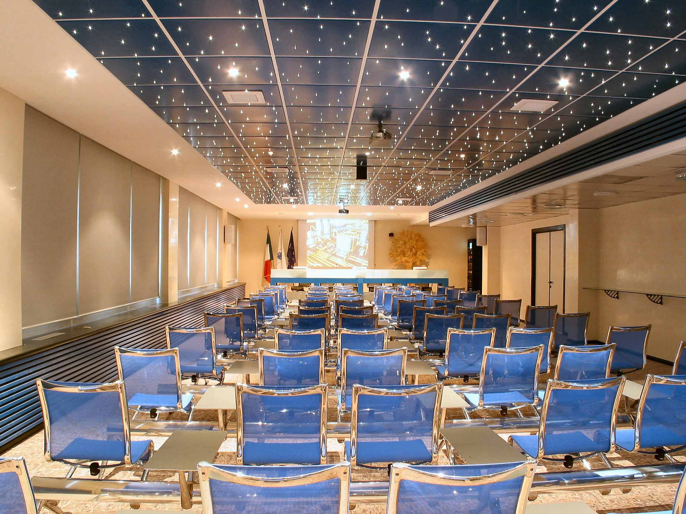 Sala meeting Foppa Pedretti con sedute blu, soffitto cielo stellato e schermo di proiezione