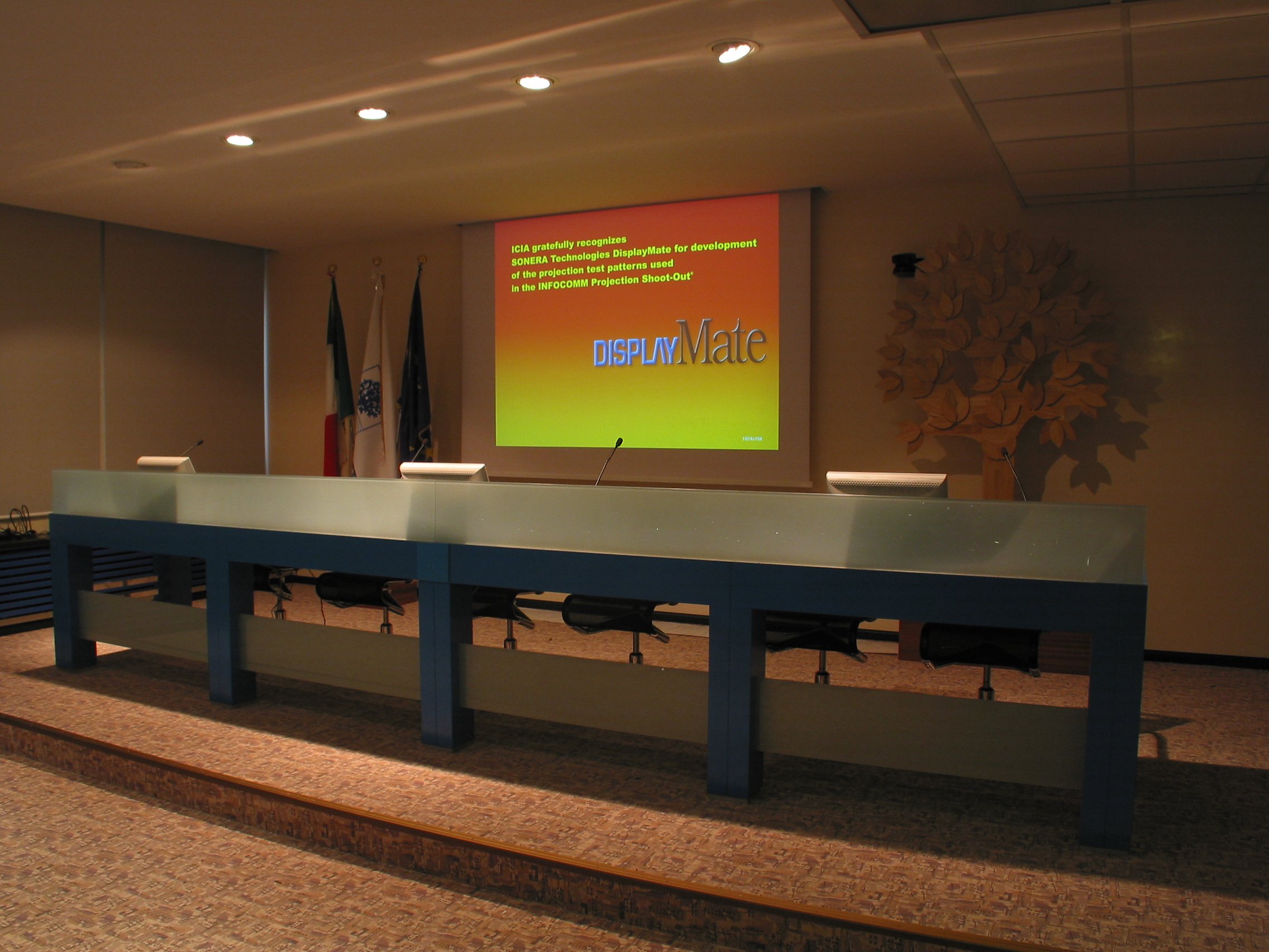 Banco relatori con schermo di proiezione e bandiere nella sala meeting Foppa Pedretti