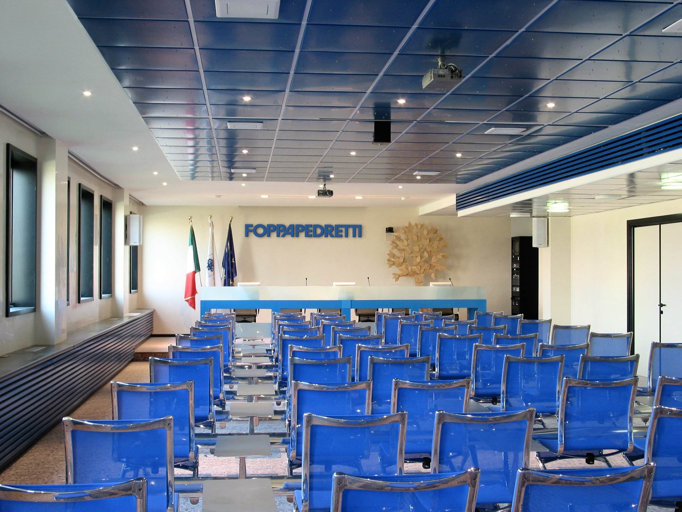 Sala conferenze Foppa Pedretti con logo aziendale, controsoffitto acustico e sedute blu
