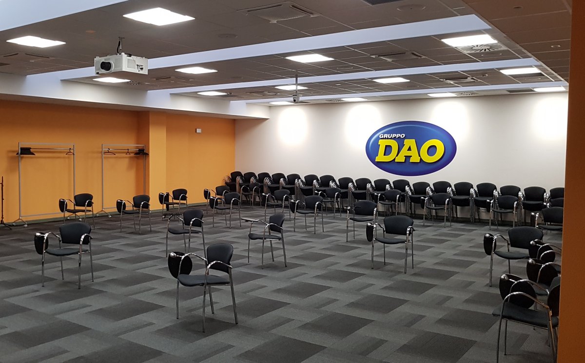 Sala assemblee Gruppo DAO vista laterale con logo, proiettore e sedute nere