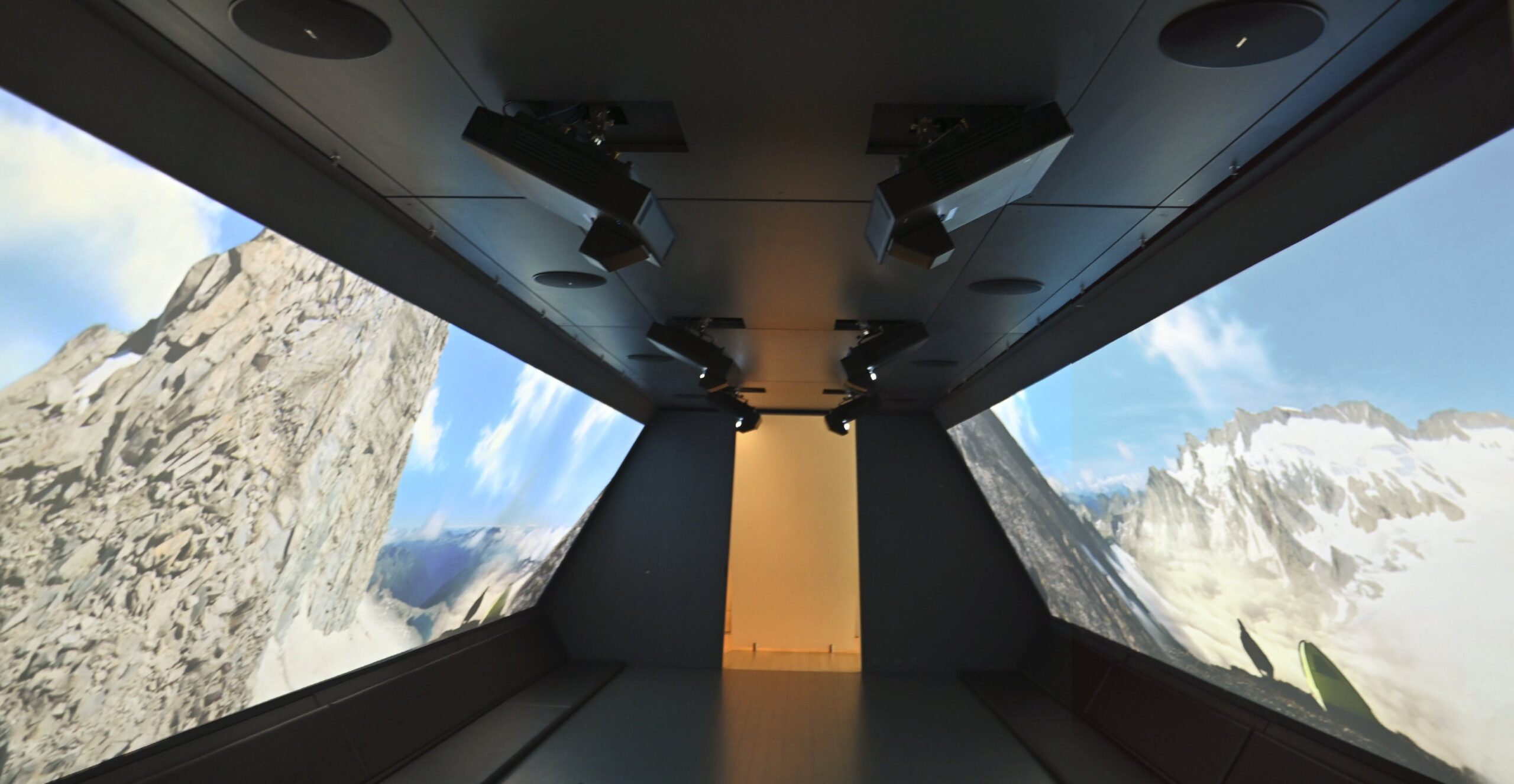 Corridoio immersivo al MUSE di Trento con proiezioni di montagne su pareti laterali e proiettori