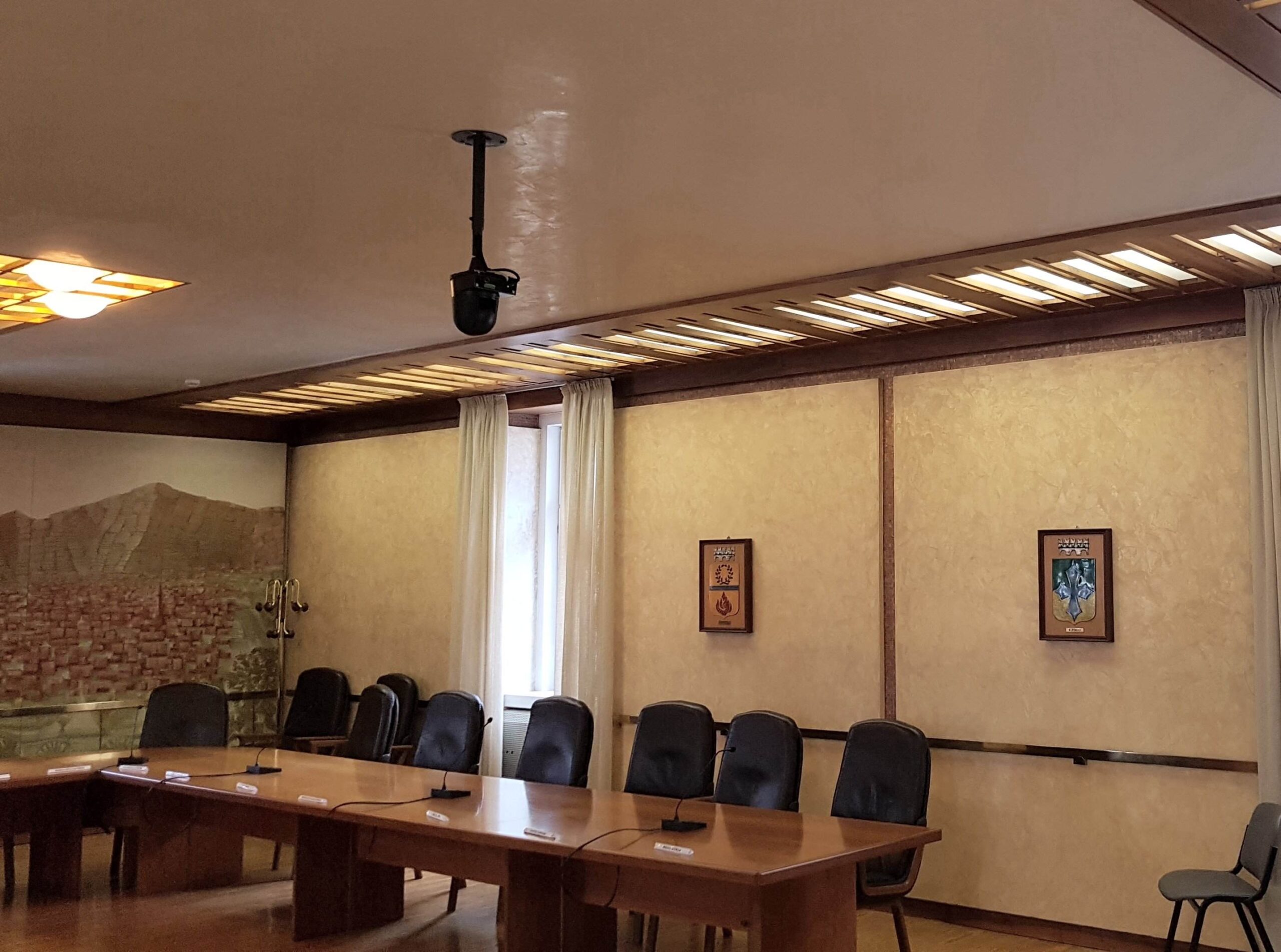 Telecamera PTZ a soffitto e postazioni con microfoni nella sala consigliare di Tione