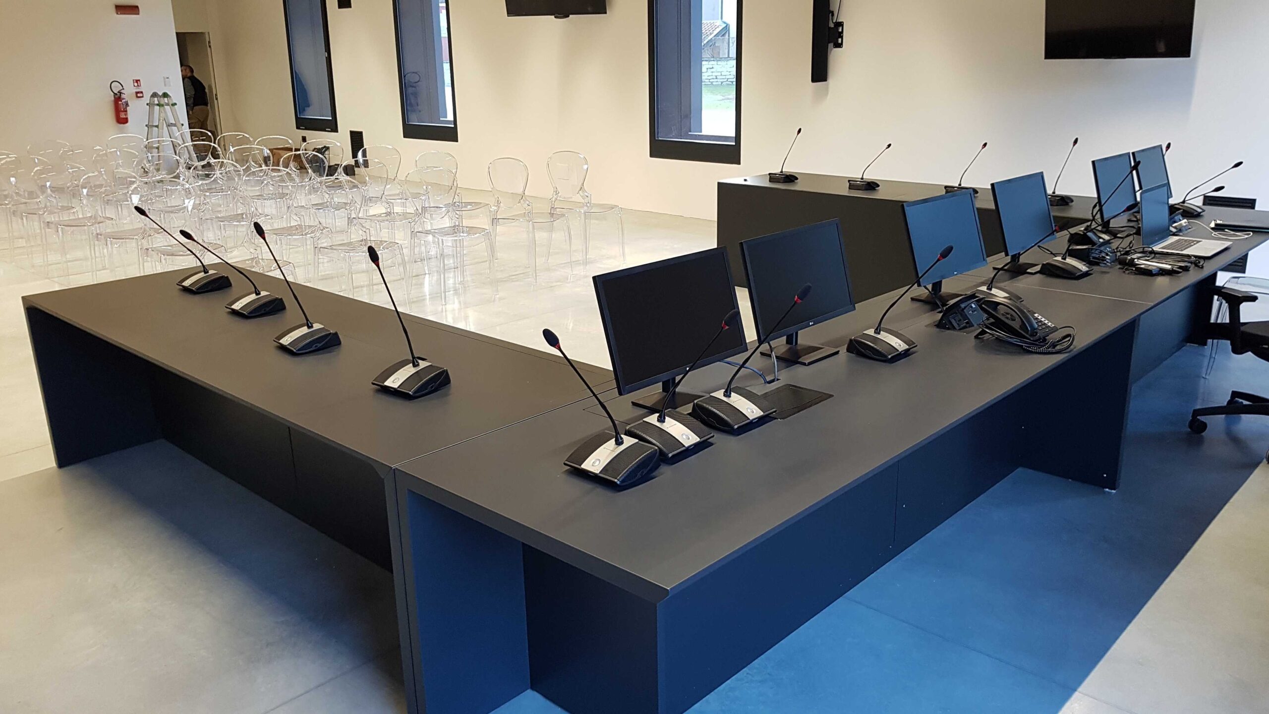 Tavolo consigliare con monitor, microfoni Sennheiser e sedie nella sala di Torbole
