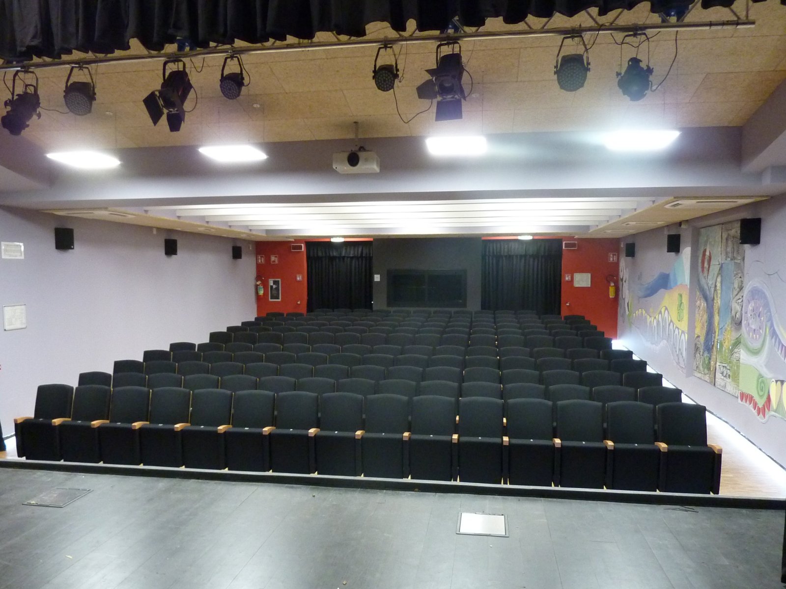 Platea con poltrone blu e palcoscenico con luci teatrali nella sala polifunzionale di Gardolo