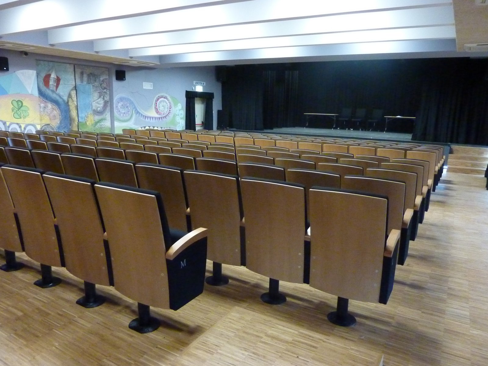 Vista laterale della platea con poltrone in legno e palcoscenico nella sala polifunzionale di Gardolo
