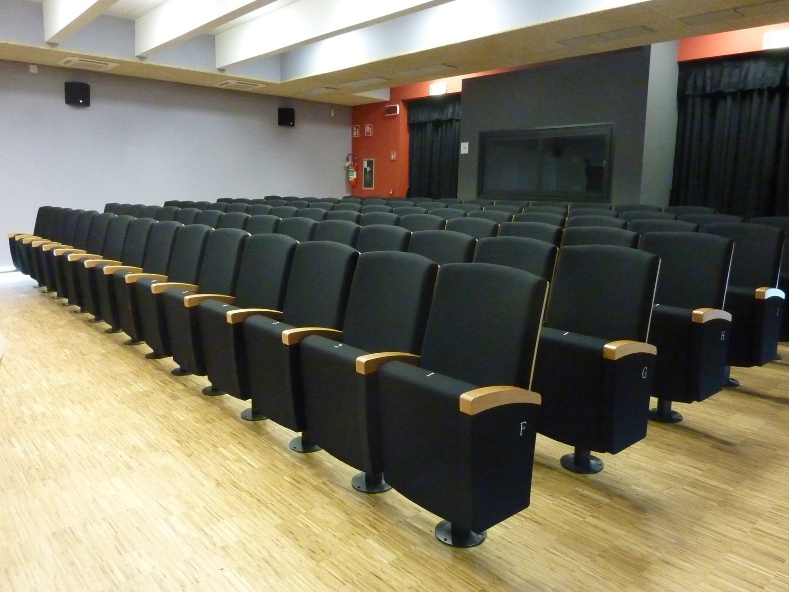 File di poltrone nere imbottite con diffusori audio a parete nella sala polifunzionale di Gardolo
