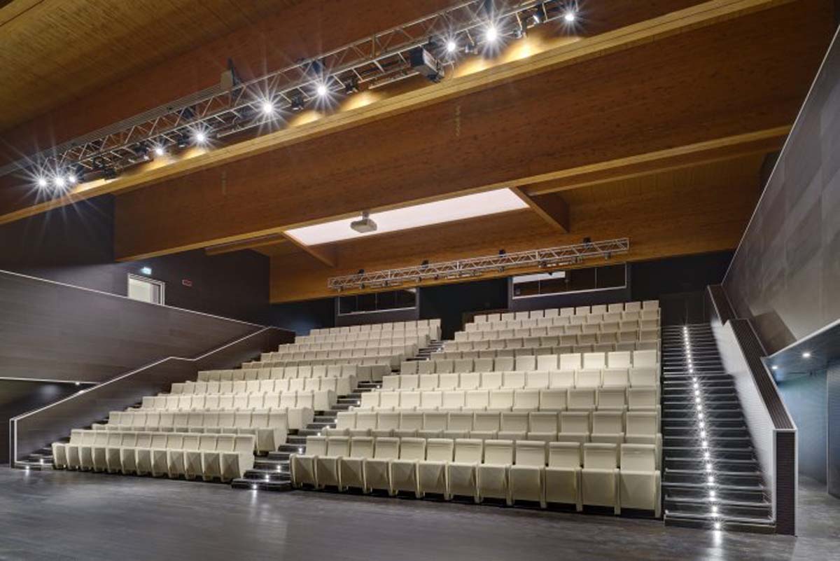 Auditorium Sanbapolis con gradinata di poltrone chiare, tralicci luci e soffitto in legno
