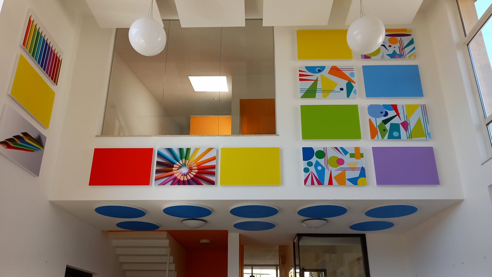 Parete a doppia altezza con pannelli fonoassorbenti colorati e dischi blu nella scuola di Ville d'Anaunia