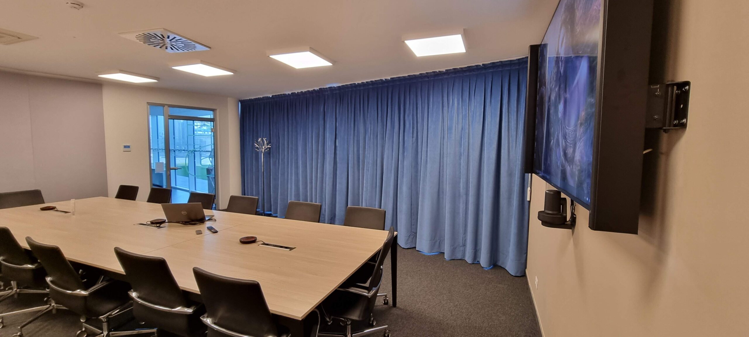 Sala riunioni Solid Power Pergine con tende fonoassorbenti blu, display a parete e tavolo conferenze
