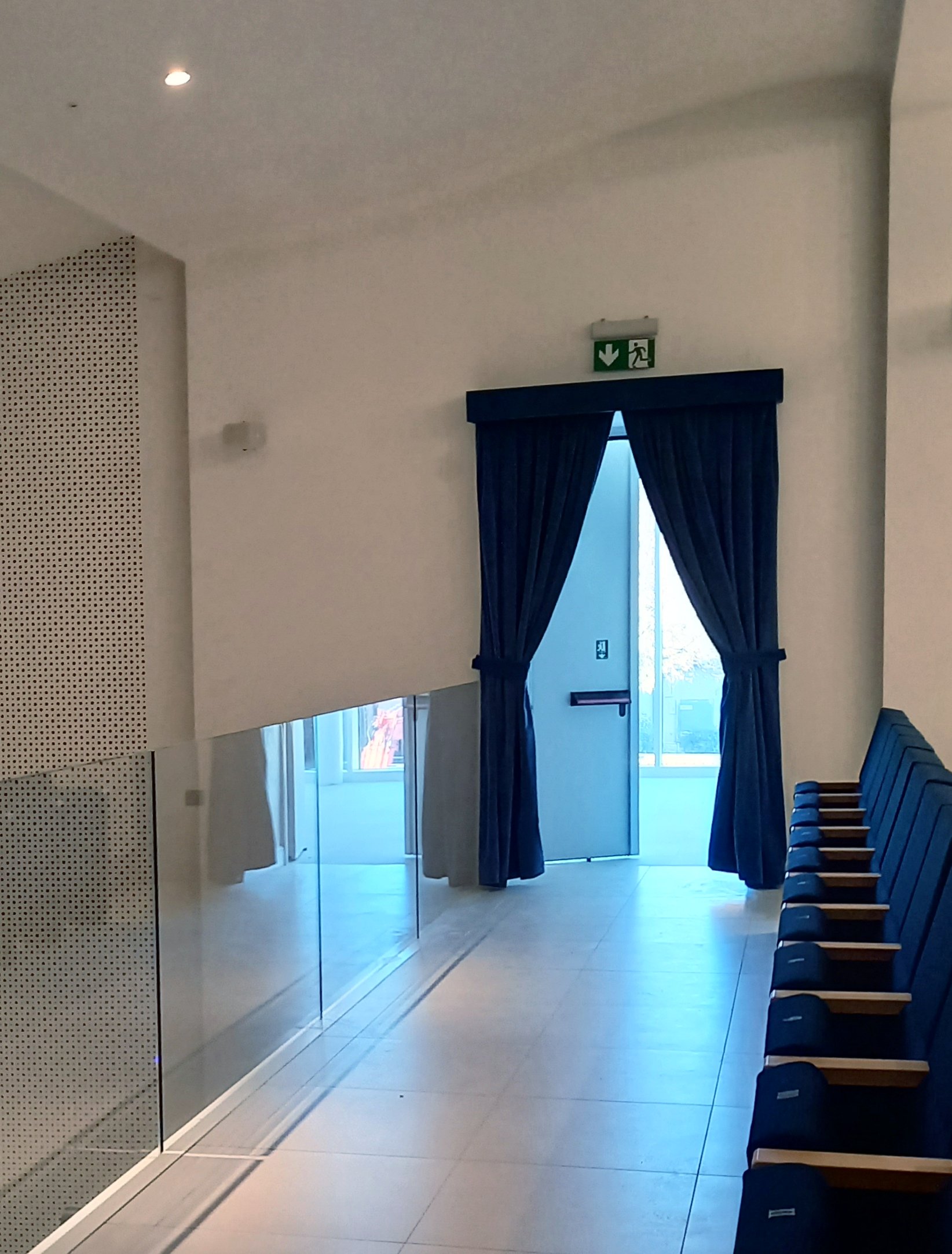 Uscita di sicurezza del teatro di Calcinato con tende oscuranti, pannelli forati e poltrone laterali
