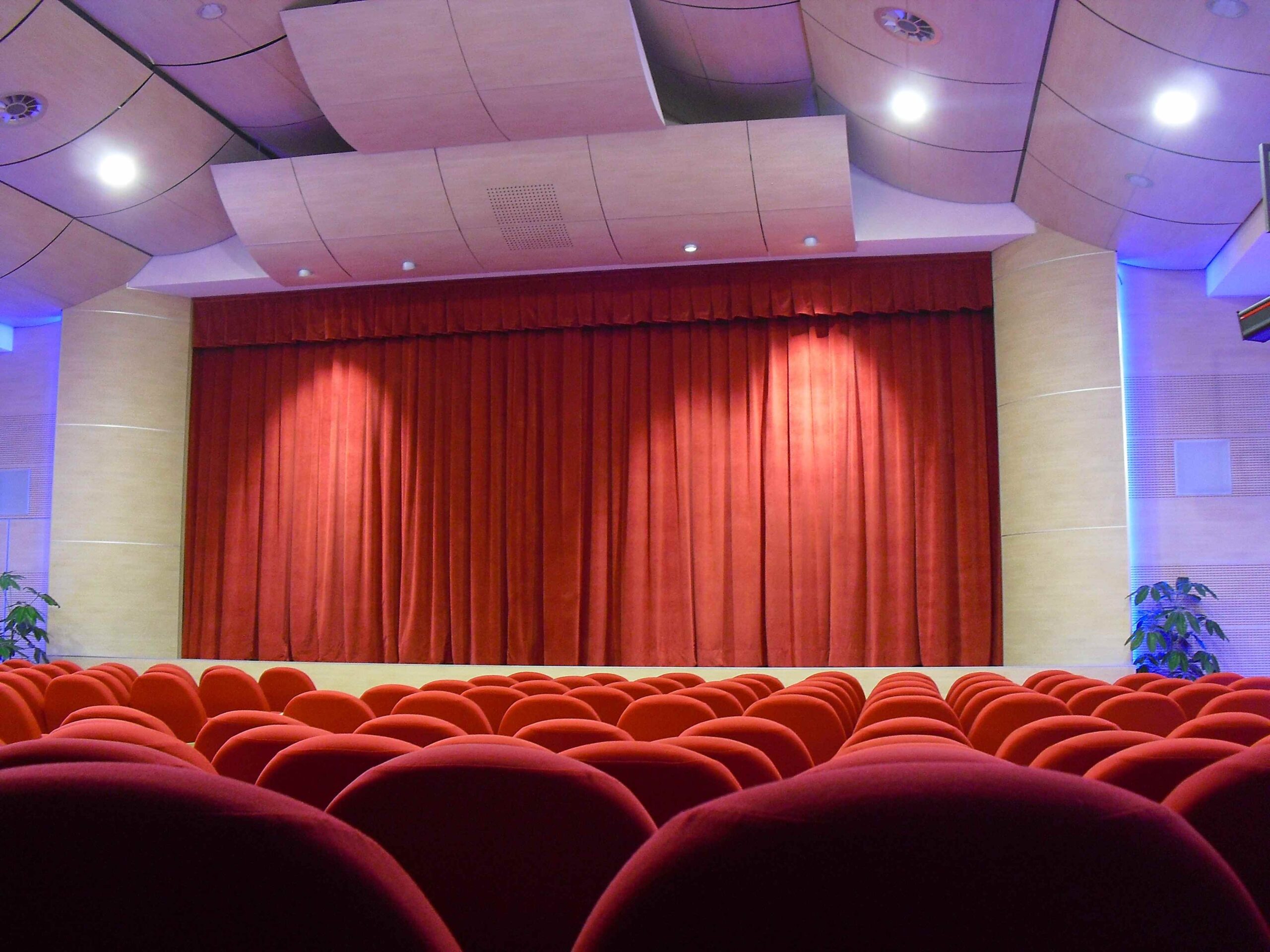Sipario rosso illuminato e poltrone rosse del teatro di Igea Marina con pannelli acustici a soffitto
