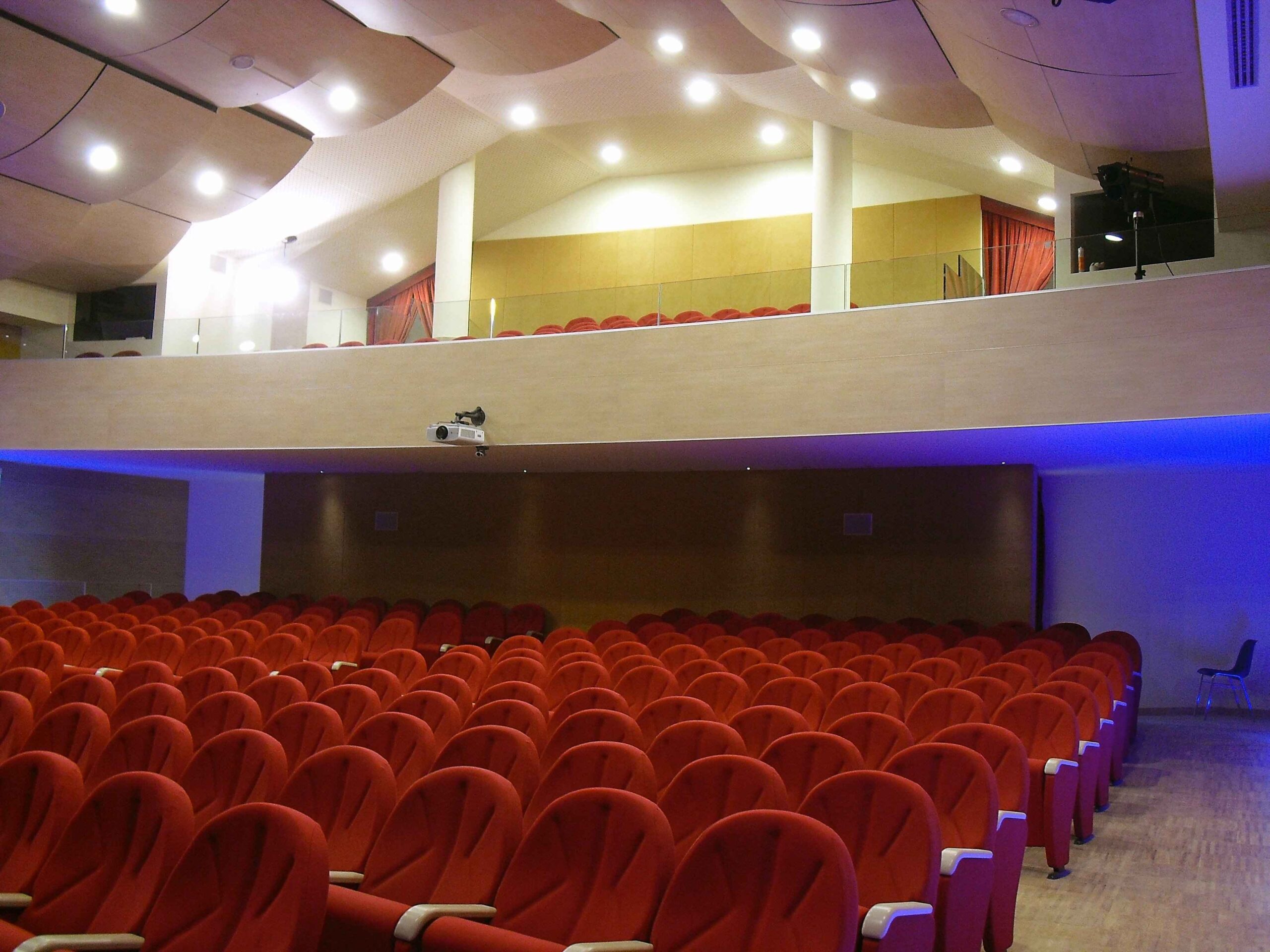 Platea e galleria del Teatro di Igea Marina con poltrone rosse, proiettore e pannelli fonoassorbenti a soffitto