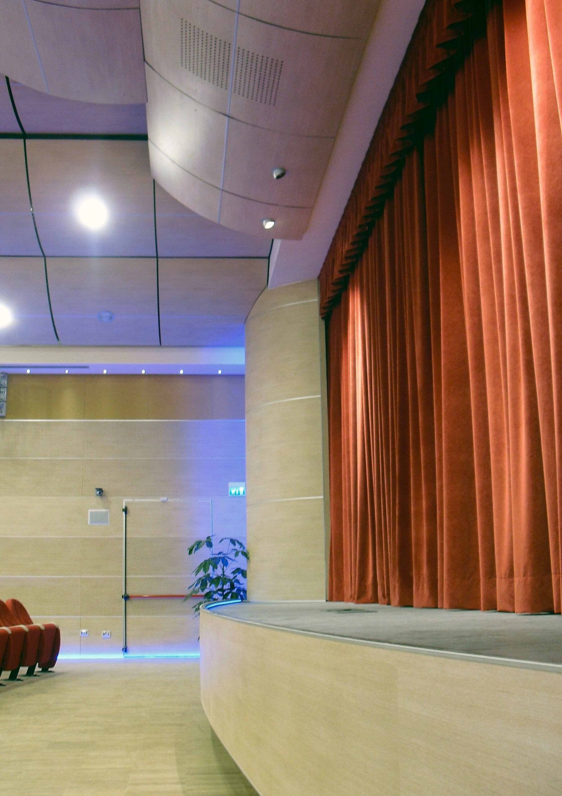Lato palcoscenico con sipario rosso, pannelli acustici e illuminazione LED blu al Teatro di Igea Marina