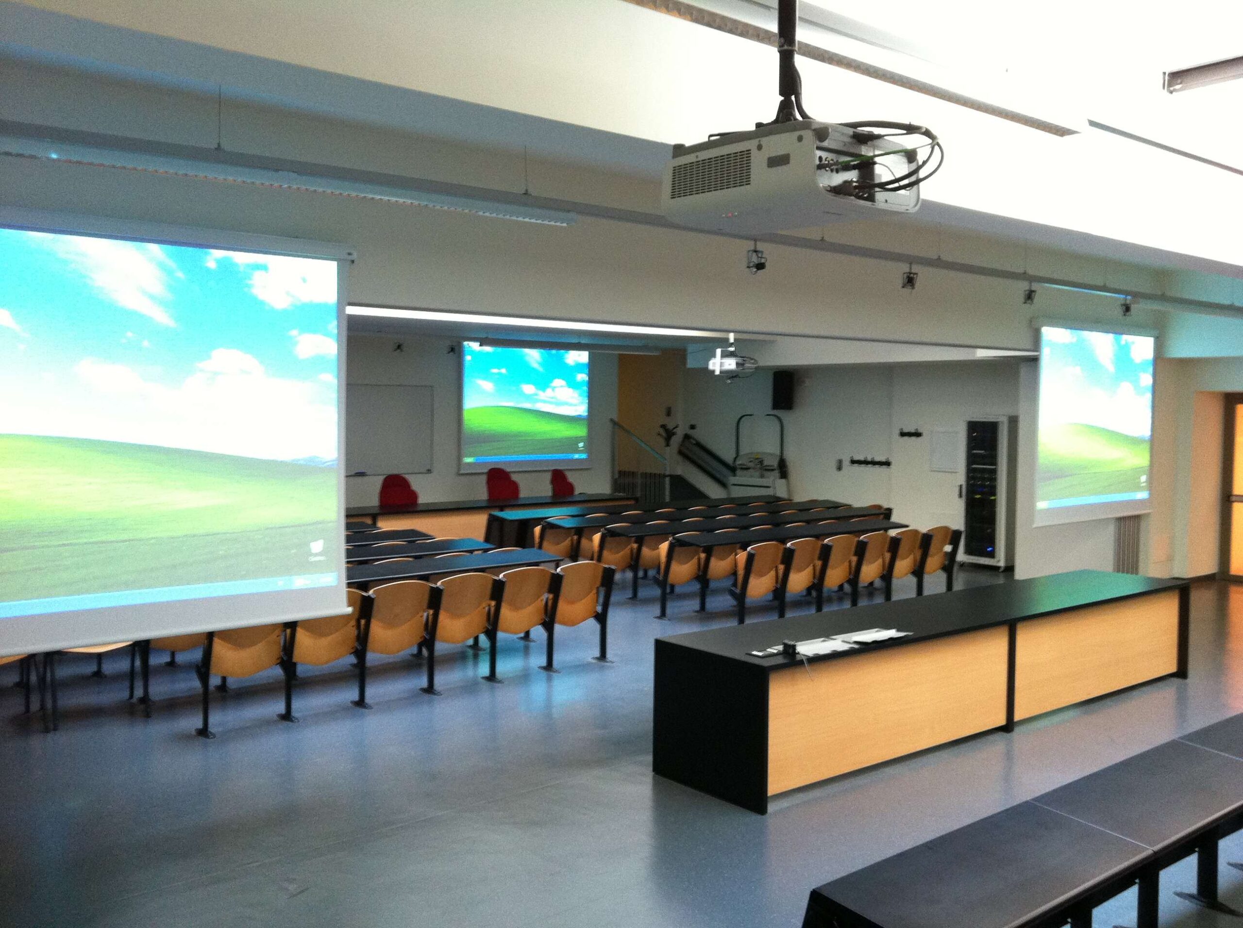 Aula magna dell'Universita di Trento con triplo schermo di proiezione, proiettore e postazioni docente