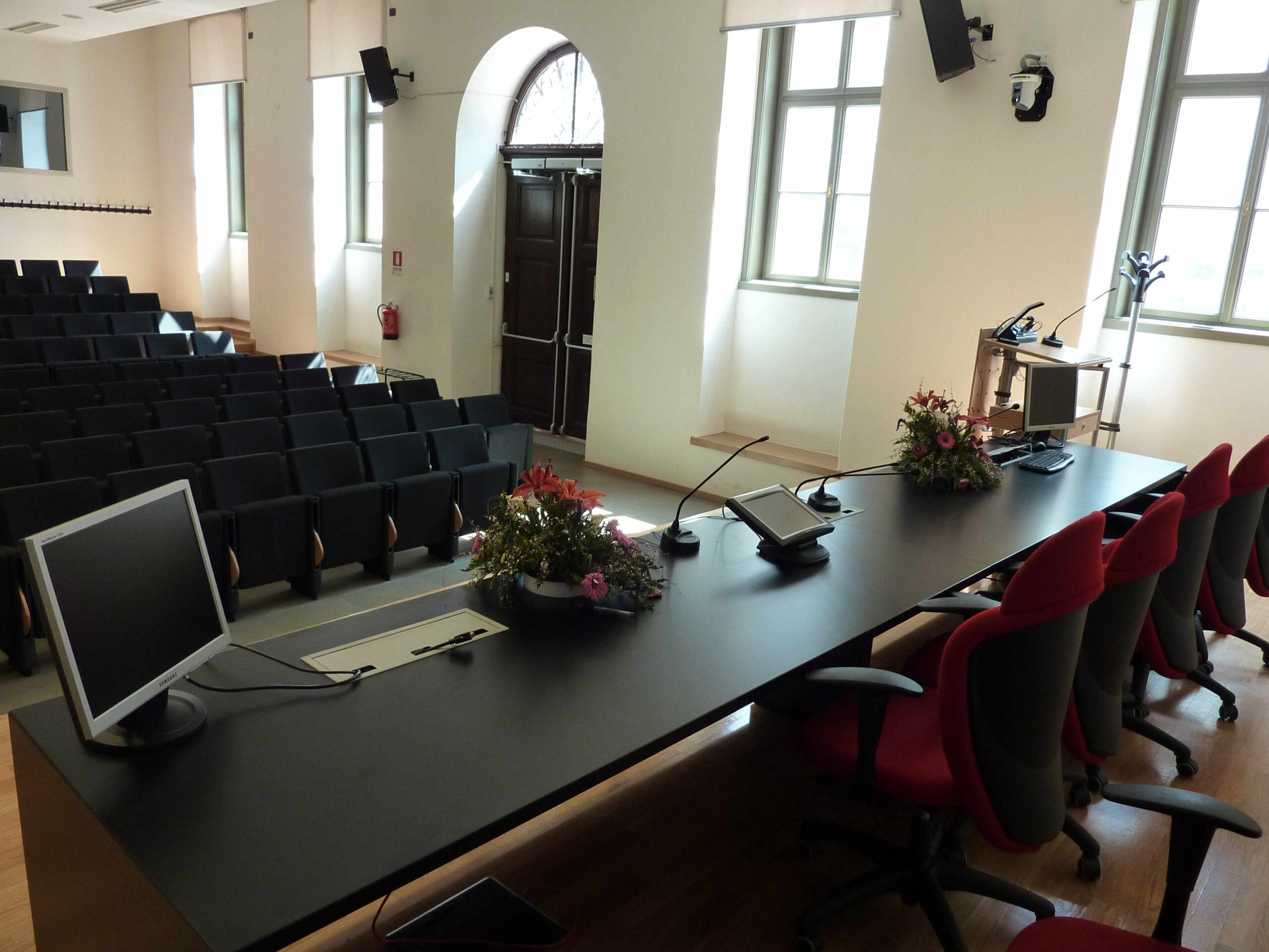 Tavolo relatori con microfoni, monitor e diffusori audio nella sala conferenze dell'Universita di Trento