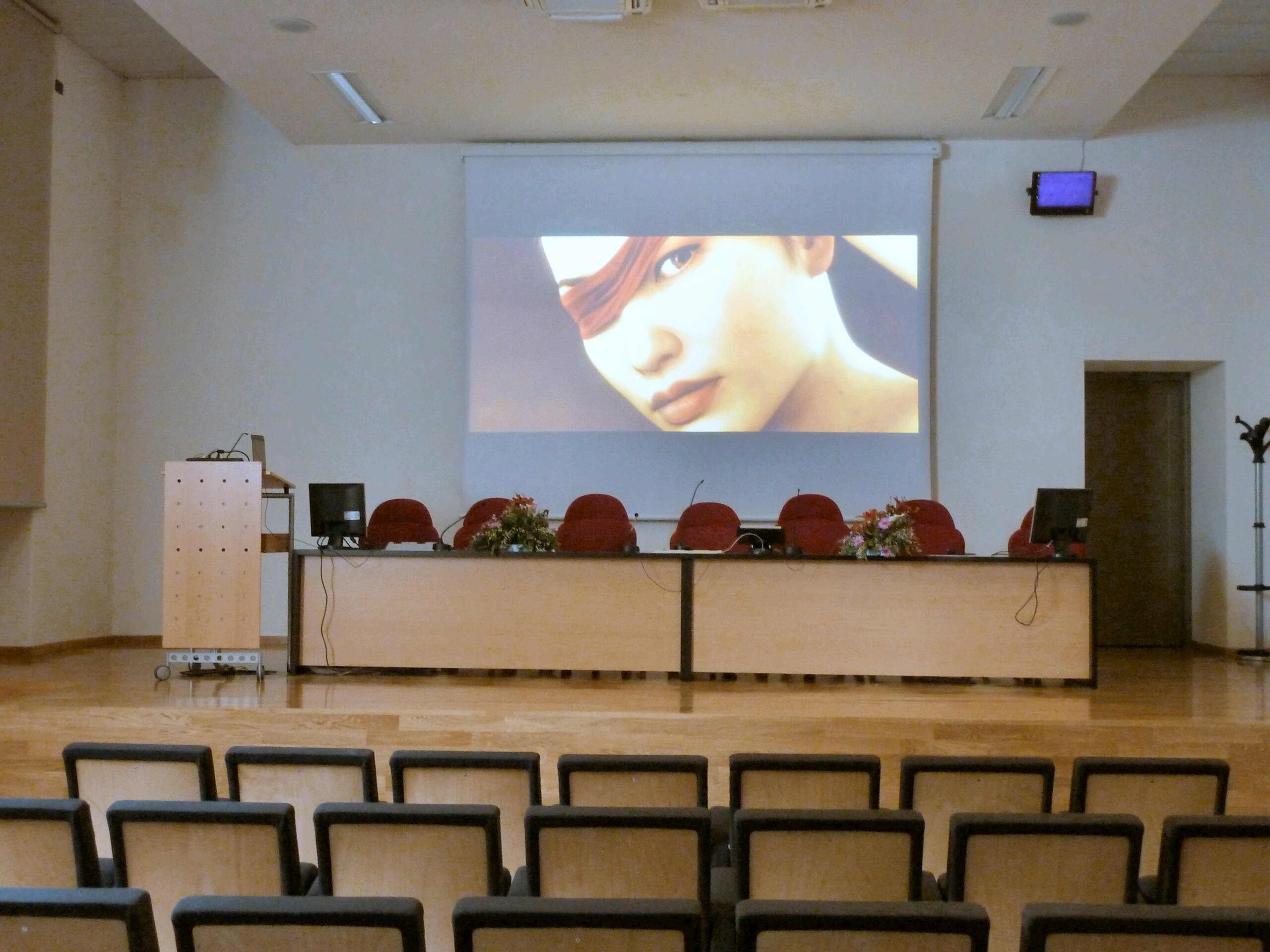 Sala conferenze dell'Universita di Trento con schermo di proiezione attivo, tavolo relatori e sedute