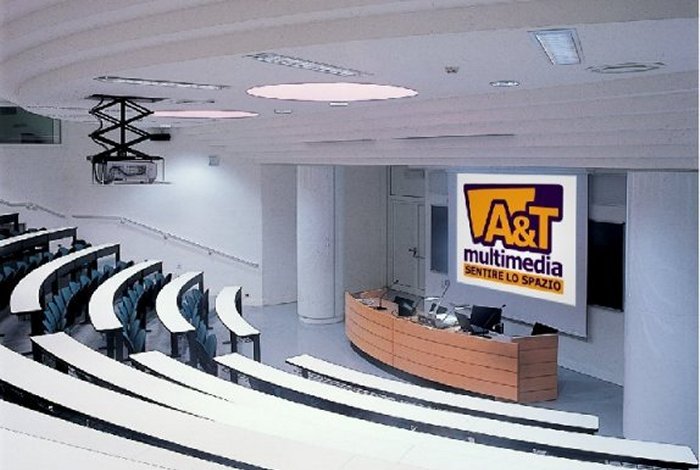 Aula universitaria a gradoni dell'Universita di Trento con schermo proiezione e logo A&T Multimedia